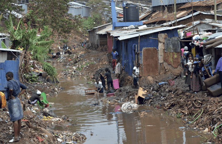 A group of people standing in a stream with informal settlements either side.