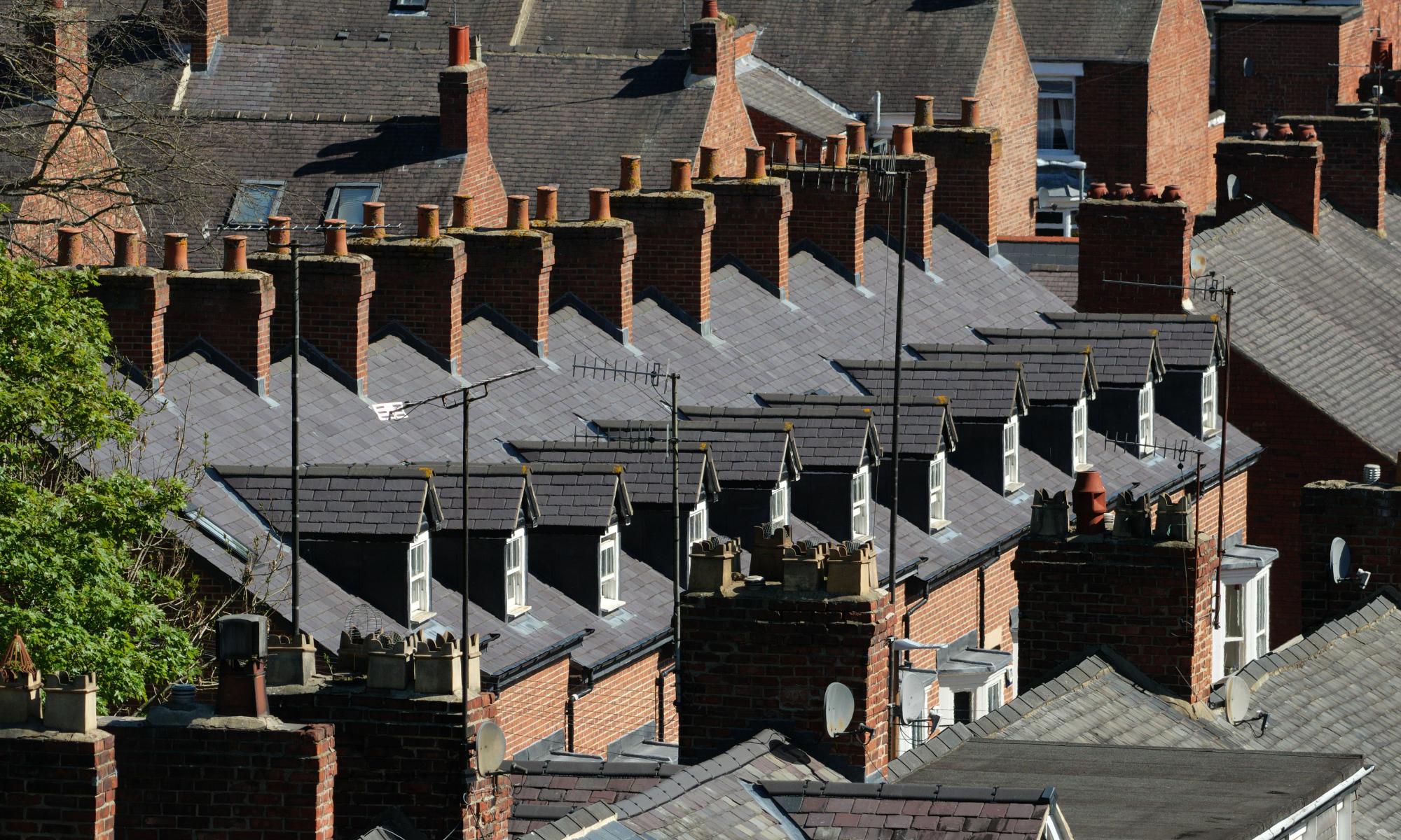 Row of traditional red brick terraced houses with slate roofs and multiple chimneys under bright daylight.