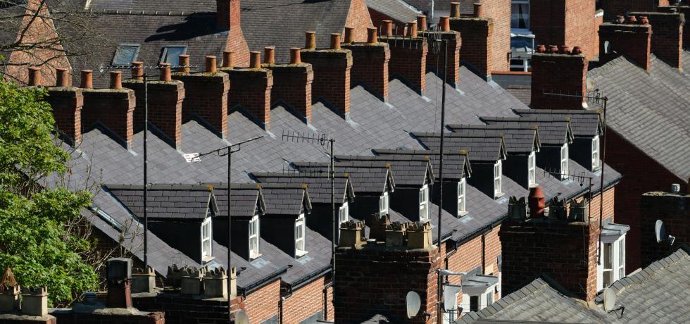 Row of traditional red brick terraced houses with slate roofs and multiple chimneys under bright daylight.